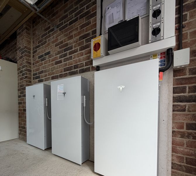 Finished Artisan Electrics installation showing one Tesla Powerwall 3 leader unit flanked by two DC Expansion Packs in a UK home garage — rear cabling and DC connection harness visible between units
