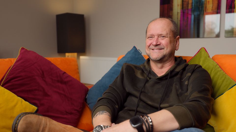 Karl Vasko smiling during his Artisan Electrics customer testimonial — Tesla Powerwall 3 units visible behind him against brick wall